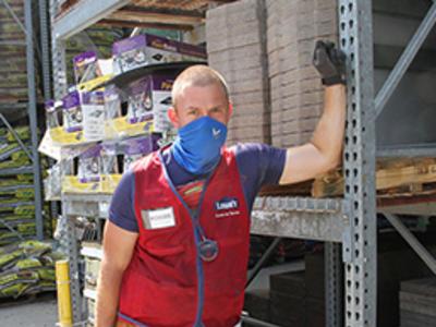 A Lowes employee stands in the garden center and looks at the camera with a blue mask on