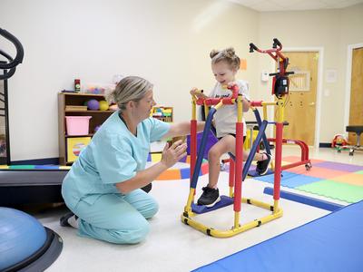 A child is running on a physical therapy device while a therapist assists