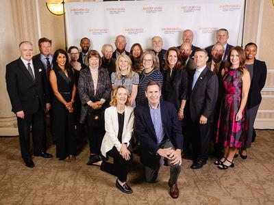 A large group of well-dressed people standing in front of a step and repeat