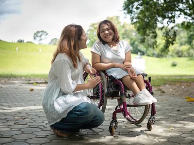 Two women are speaking to each other. One woman is in a wheel chair and the other woman is kneeling beside her.