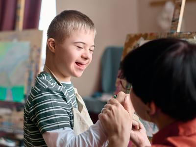 A boy with Down syndrome is enjoying painting in an art class