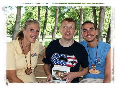 A camp director and counselor sit on either side of a man with a disability at a Campground