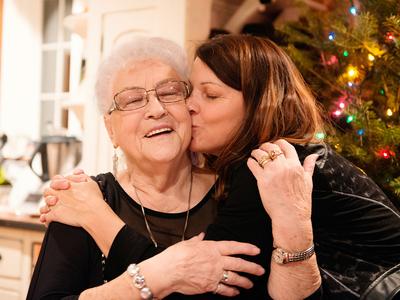 Daughter kiss elderly mother with a christmas tree in the background. The mother is smiling.