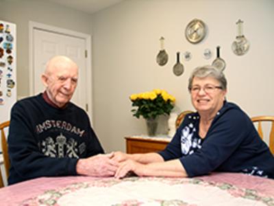 Older couple sits at dining room table and hold hands