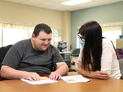 Man with a disability sits at a table with his direct support professional