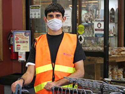 Employee wearing a mask is wearing an orange vest and has his hands resting on shopping carts