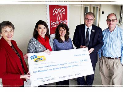 five adults stand in front of an Easterseals sign while holding a large check