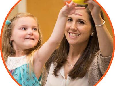 Child reaching for a yellow toy as her therapist works with her