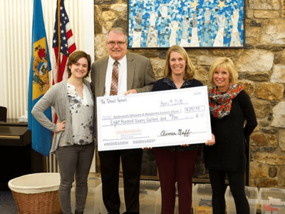 Four people stand in front of a stone wall presenting a check to the camera. 