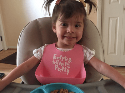 Smiling Toddler girl with brown pig tails in highchair with pink bib