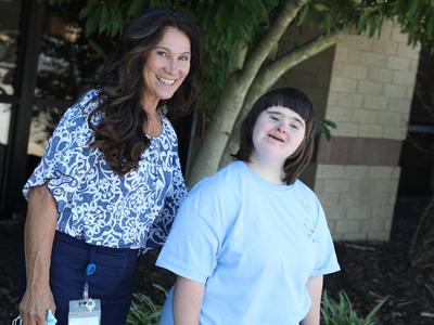 two adult females outside by a tree one with long brown hair and one with down syndrome and short brown hair enjoying the breeze  