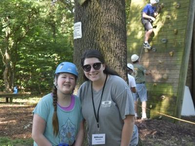 Adolescent girl with blue helmet on standing next to camp counselor female with brown hair