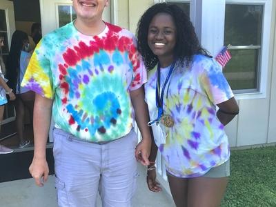 Young adult male with a disability wearing a tie dye tshirt standing with camp counselor