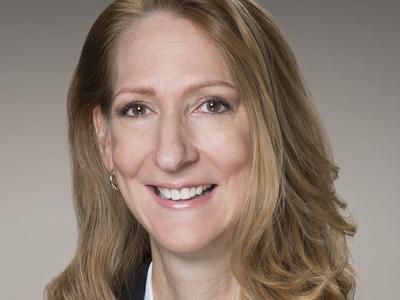 A Headshot of a woman with long hair. She is wearing a black blazer.