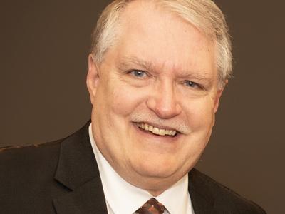 A headshot of a man with an orange tie and black blazer