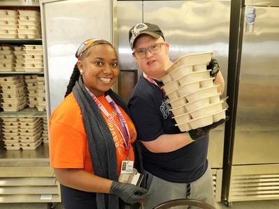 A support professional stands next to a man with a disability who is transferring food from a freezer