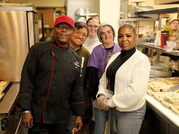 A group of people stand in a kitchen and they are all smiling at the camera