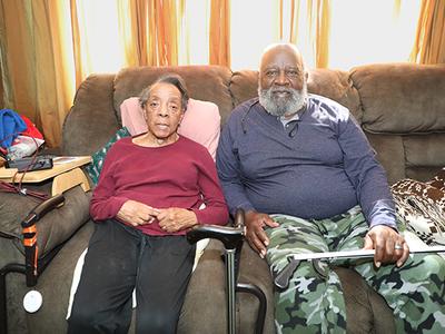 An older couple sits on a couch and looks at the camera