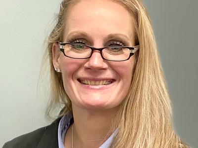 A headshot of a woman wearing glasses and long blond hair. She is smiling at the camera.