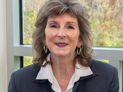 A headshot of a woman wearing a blazer sitting in front of an open window.