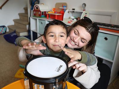 A child with autism play a drum with the assistance of a therapist