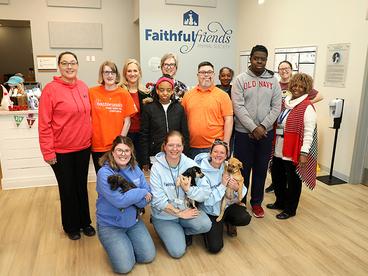 A group of people and dogs stand in an animal rescue center and smile at the camera.