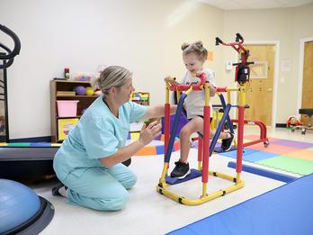 A child is running on a physical therapy device while a therapist assists