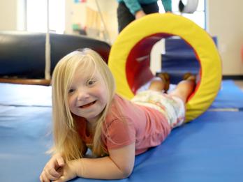 Young girl with blond hair on a play matt in physical therapy