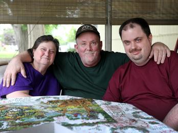 Older parents sitting at a table doing a puzzle with their adult son that has a disability