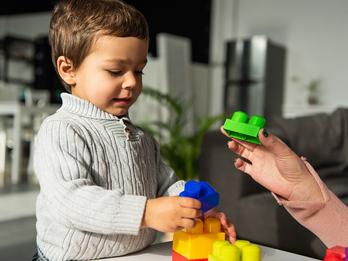 A small child is playing with large legos as a person off screen assists