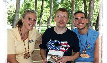 A camp director and counselor sit on either side of a man with a disability at a Campground