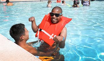 A man with a disability is swimming in a pool with the assistance of his counselor